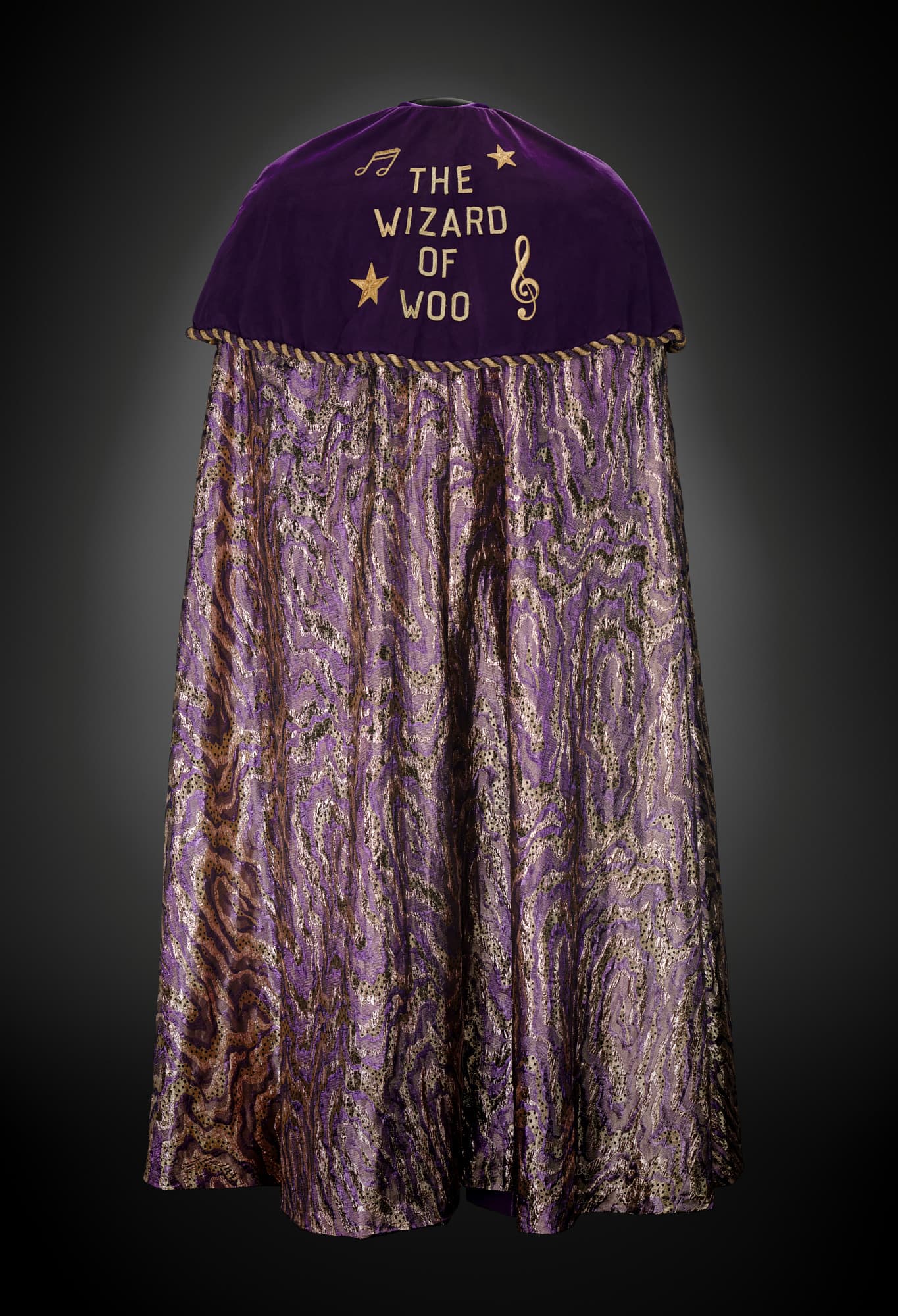 a purple cape with gold musical notes and stars stitched in and the words "The Wizard of Woo"